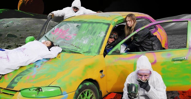 schauspielende in Maleroveralls stehen rund um ein bunt bemaltes Auto