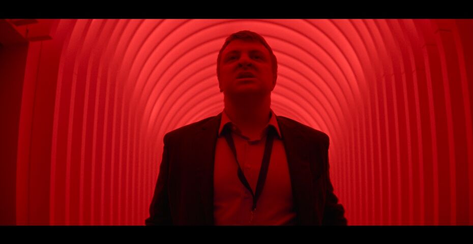 Ein Mann mit Hemd, Jacket und aufgeknöpfter Krawatte steht in einem rot angeleuchteten Tunnel